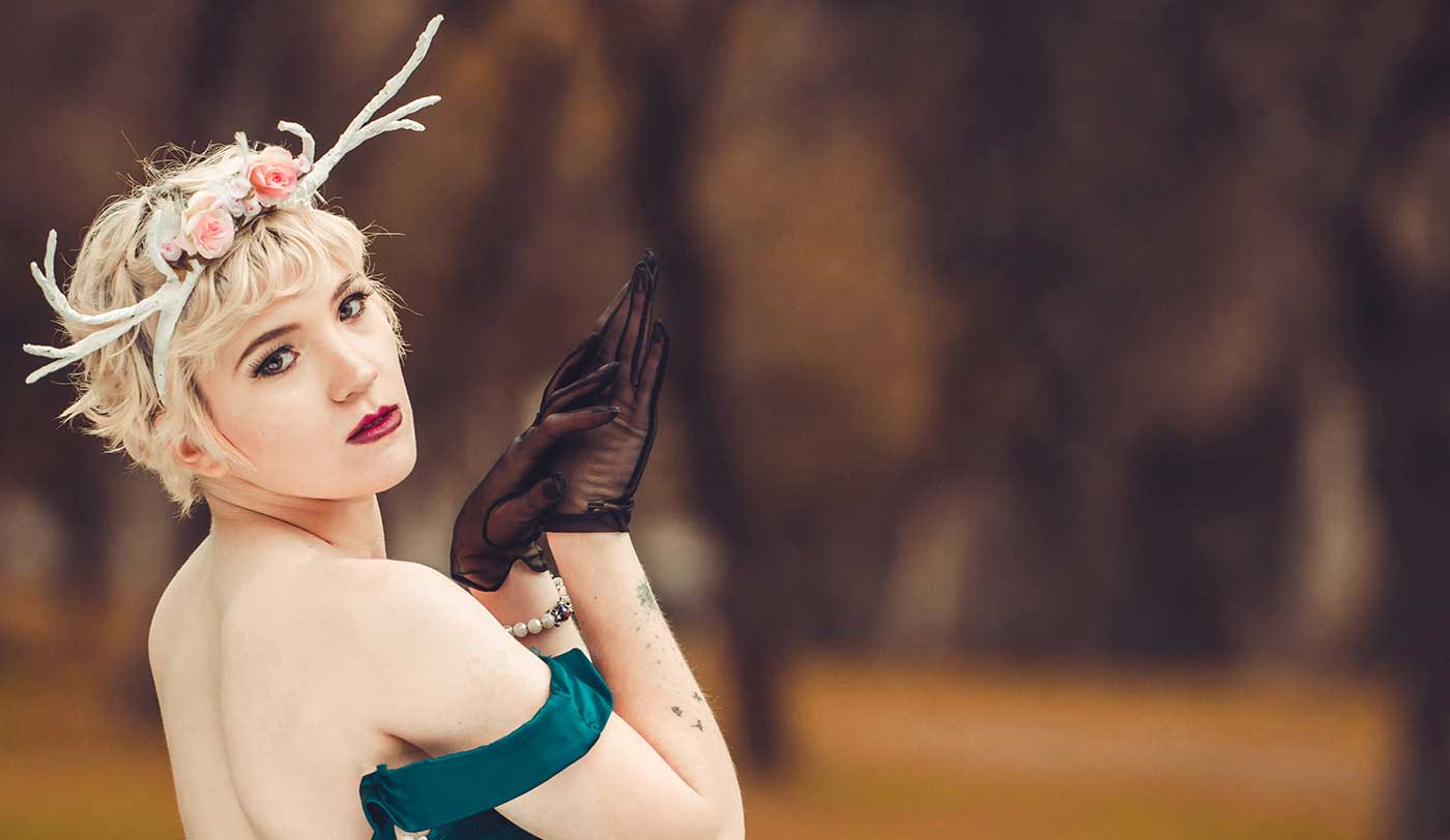 Fotografía de mujer rubia con bincha de cuerno  de ciervo posando en un bosque otoñal