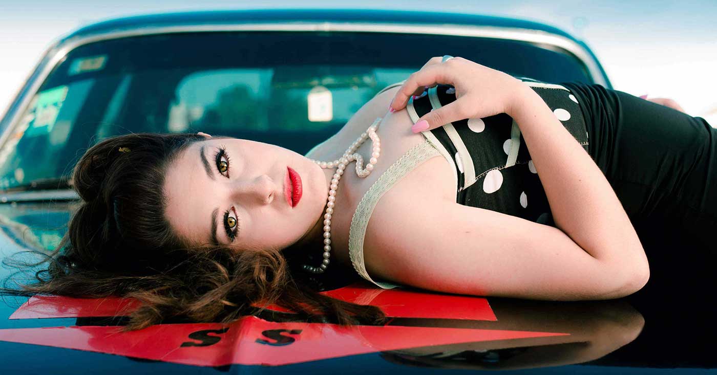 Fotografía de modeo ambientada en los años 70recostada sobre automovil antiguo